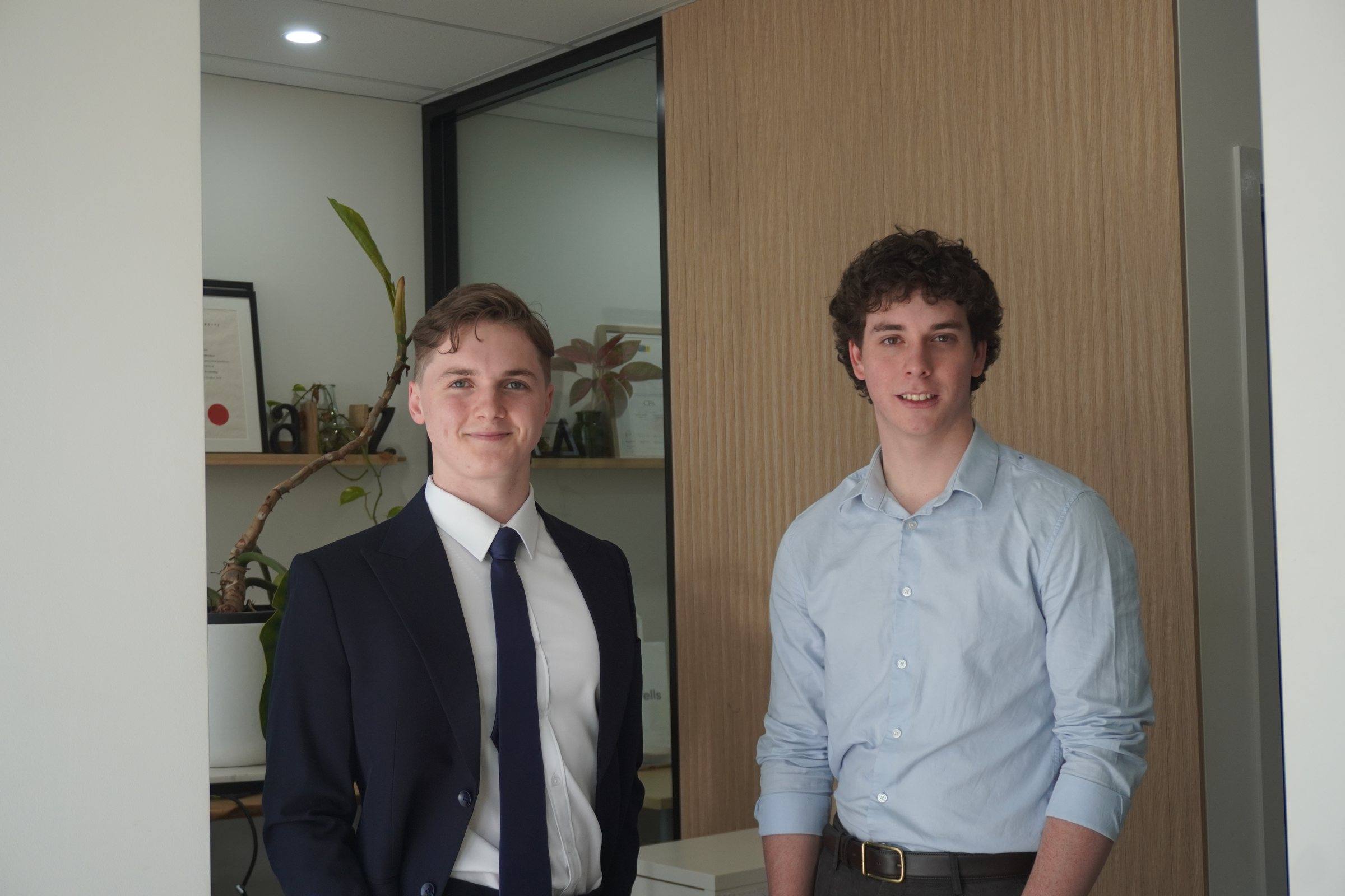 Zeek in a navy suit and Levi in a light-blue shirt, standing together in their office