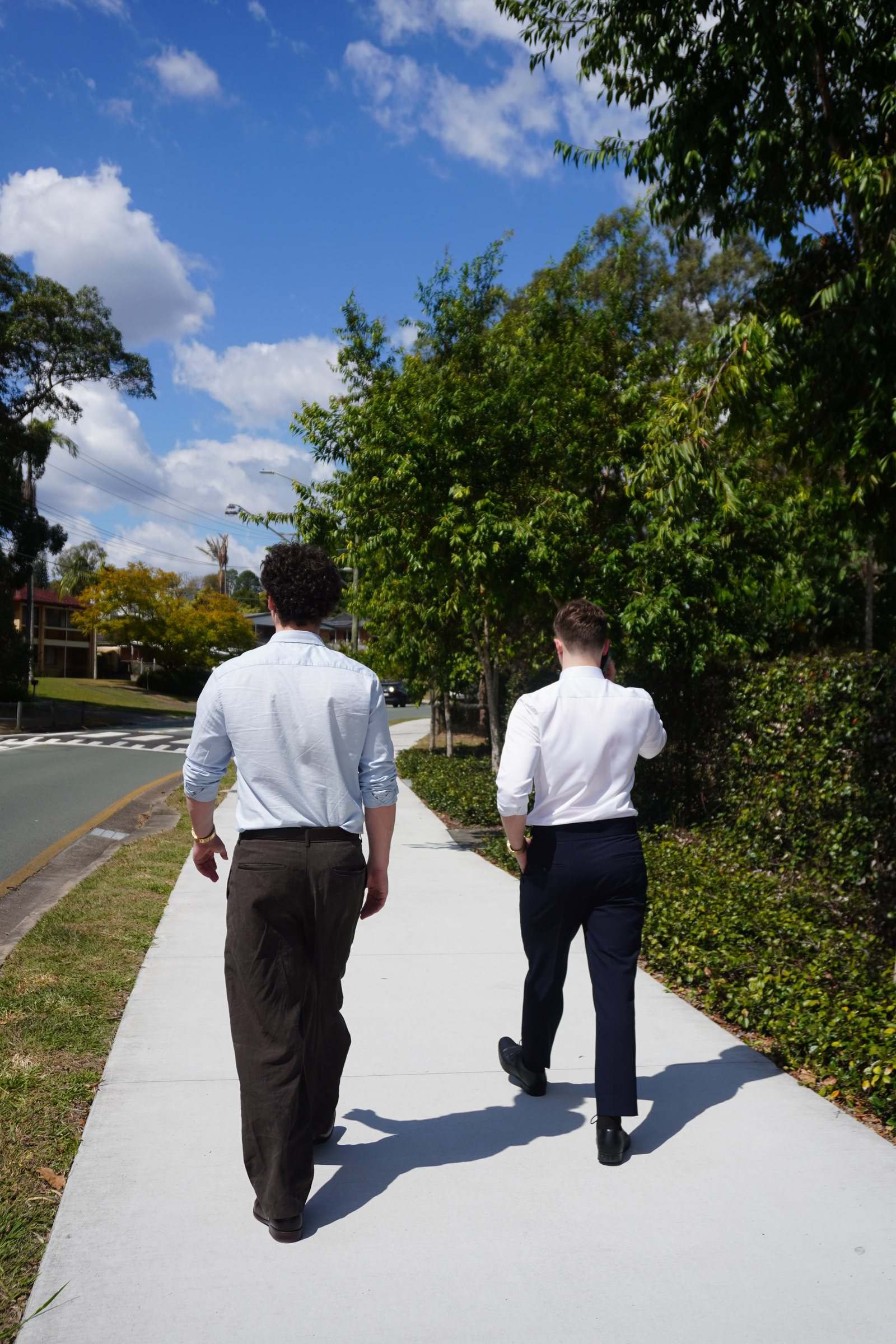 Levi and Zeek walking away down a sunny suburban footpath
